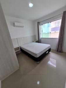 uma cama num quarto com uma janela em Amplo e aconchegante apartamento com 3 quartos a 50m da praia de Bombas em Bombinhas
