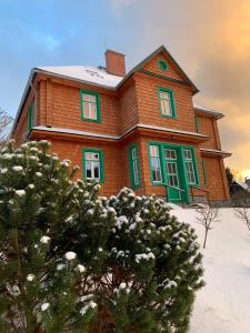 a brown house with green windows in the snow at Chata Klášter in Hraběšice