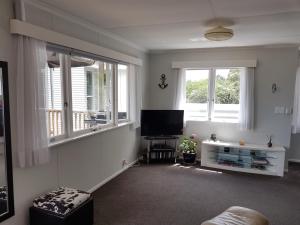uma sala de estar com televisão e duas janelas em Coromandel Tapu - Beachfront Escape em Tapu