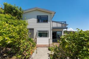 a white house with a balcony and some bushes at Ocean Spa Views in Nelson