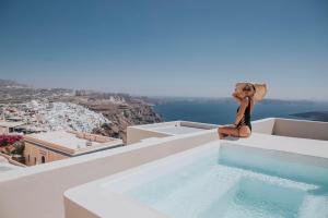 una mujer sentada en el borde de una piscina en Caldera Cliff Illusion, en Fira