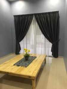 a wooden table in front of a window with curtains at afza homestay Bonda Bukit Besi in Kampong Kuala Talam
