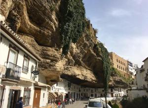 a stone mountain next to a street with buildings at Casa Rural Cuevas del Sol in Setenil