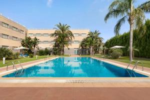 a swimming pool in front of a building with palm trees at Ramada by Wyndham Valencia Almussafes in Almussafes