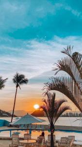 uma praia com cadeiras e uma palmeira e o pôr do sol em Ilha Porchat Hotel em São Vicente
