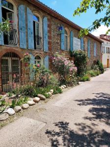 un bâtiment en briques avec des fenêtres bleues et des fleurs devant lui dans l'établissement Domaine de la Tannerie les Coulisses, à Prades