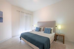 um quarto branco com uma cama grande e almofadas azuis em Fábrica da Ribeira 54 by Destination Algarve em Lagos