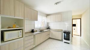 cocina con armarios de madera, microondas y electrodomésticos en Ótimo imóvel a duas quadras do café curação, en Guaratuba