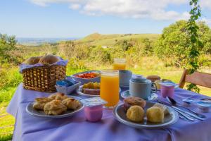 a table with a blue table cloth with breakfast foods and orange juice at Pousada Gaya in Carrancas