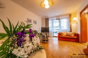 Una sala de estar con un jarrón de flores moradas y blancas. en Baltic Apartments - Zdrojowa, en Świnoujście