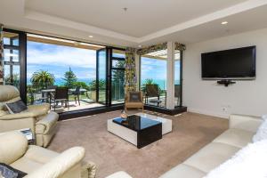 een woonkamer met een tv en grote ramen bij Silver Sands - Beachside Apartment in Nelson