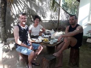 tres hombres sentados alrededor de una mesa con comida. en B & B CHARM, en Dikwella