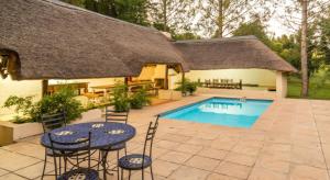 a house with a pool and chairs and a thatch roof at Pine Valley in Lanseria