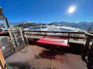 une table rouge sur un balcon avec vue sur une montagne enneigée dans l'établissement appartement en duplex alpe d'huez, à L'Alpe-d'Huez