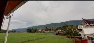 a large green field with houses and mountains in the background at Toba Boi in Tuk Tuk