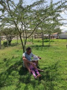 una mujer y un niño sentados en la hierba bajo un árbol en Achab Eco cabin, en Usakos
