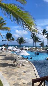 una piscina con sillas, sombrillas y palmeras en Beach Class Muro Alto Porto de Galinhas, en Porto de Galinhas