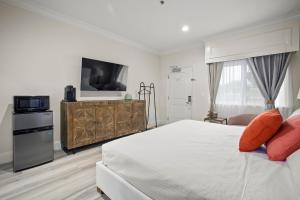 a white bedroom with a bed and a tv at Hotel Huntington in Duarte