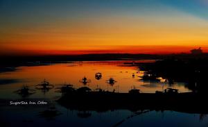 un coucher de soleil sur une étendue d'eau avec des bateaux. dans l'établissement Sugarsea Inn & Dive shop, à Mactan