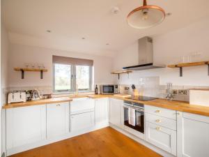 cocina blanca con suelo de madera y armarios blancos en Chestnut Cottage, en Winchcombe