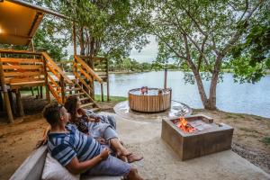 een groep mensen die rond een vuurplaats bij het water zitten bij AfriCamps Hoedspruit in Hoedspruit