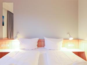 uma cama com lençóis brancos e duas almofadas em Appartement Riterspöör 24 em Westerland