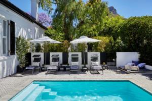 a pool with chairs and umbrellas next to a house at Kaap Mooi Luxury Guest House in Cape Town
