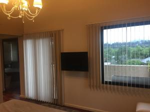 Habitación con ventana, TV y lámpara de araña. en Homestays La Reinamora en San Salvador de Jujuy