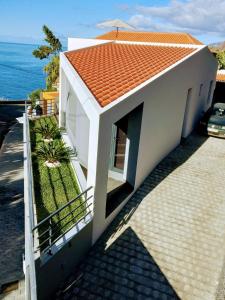 Biały dom z pomarańczowym dachem nad oceanem w obiekcie Anjos's Choice w mieście Ponta do Sol