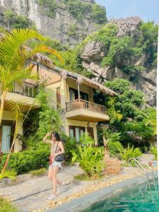 a woman walking past a house next to the water at Ninh Binh Retreat in Ninh Binh