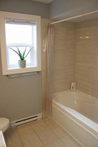 La salle de bains est pourvue d'une baignoire et d'une fenêtre avec une plante en pot. dans l'établissement Next to Olympic View golf course 2 bedroom private suite, à Victoria