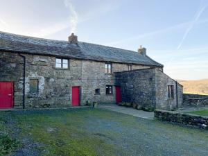 un antiguo edificio de piedra con puertas rojas en un campo en Wray Green, en Ravenstonedale