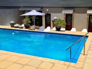 a large blue swimming pool with chairs and an umbrella at Magalies Mountain Lodge and Spa in Hartbeespoort