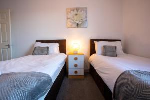 two beds in a room with a lamp on a night stand at Denecroft apartments in Lynemouth