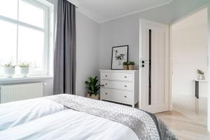 a white bedroom with a bed and a dresser at Park View Apartment przy plaży in Iława