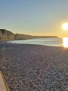 a beach with the sun setting on the water at Entre plage et port de Fécamp in Fécamp