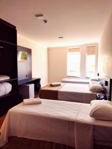 um quarto com duas camas e uma secretária e duas janelas em Hotel Itália em Paranavaí
