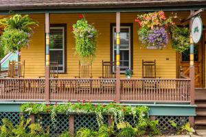 une maison jaune avec des fleurs sur la terrasse couverte à l'avant dans l'établissement Pine Cottage Bed & Breakfast, à Île Mackinac