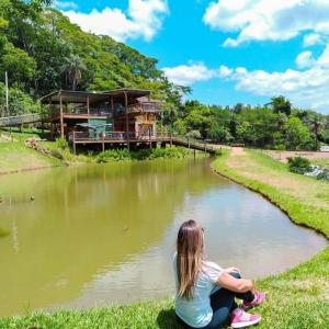 a girl sitting on the grass by a river with a house at Viva Brotas in Brotas