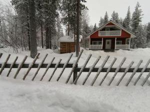 a fence covered in snow in front of a cabin at Velhonkieppi in Kittilä