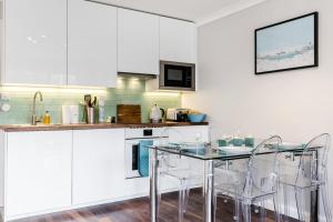 a kitchen with white cabinets and a glass table and chairs at Lovely 2 Bedroom Apartment Near South Bank in London