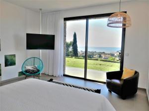 a bedroom with a bed and a chair and a large window at Appartement Regard-sur-mer 165m2 4ch vue mer piscine in Carqueiranne