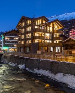 a large building next to a river with snow at Haus zur Brücke in Zermatt