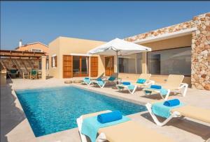 a villa with a swimming pool with chairs and an umbrella at Villas Sa Ferradura in Cala en Blanes