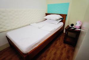 um pequeno quarto com uma cama com lençóis brancos e uma mesa de cabeceira em RedDoorz D128 Lodge Cagayan Valley em Tuguegarao City