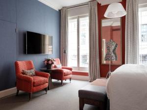 a bedroom with a bed and two chairs and a tv at Haymarket Hotel, Firmdale Hotels in London