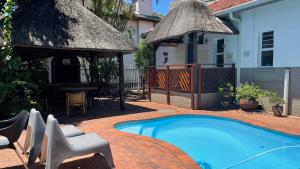 a house with a swimming pool with a thatch roof at Victorian Beach Cottages in Amanzimtoti