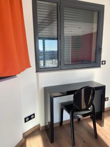 un escritorio negro con una silla junto a una ventana en La Résidence Amal en Talence