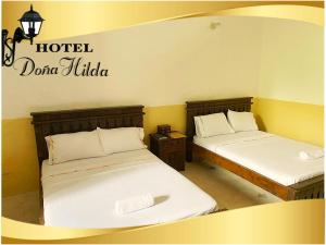 two beds in a room with a hotel sign on the wall at Hotel Doña Hilda in San Martín