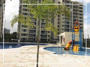 uma palmeira ao lado de uma piscina com um parque infantil em Hermoso apartamento en club house em Ricaurte